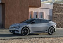 2026 Kia EV6 Gets $5,000 Price Cut as Sales Slide 46 Percent Silver 2026 Kia EV6 electric crossover parked in profile against modern brown architectural backdrop with geometric building…