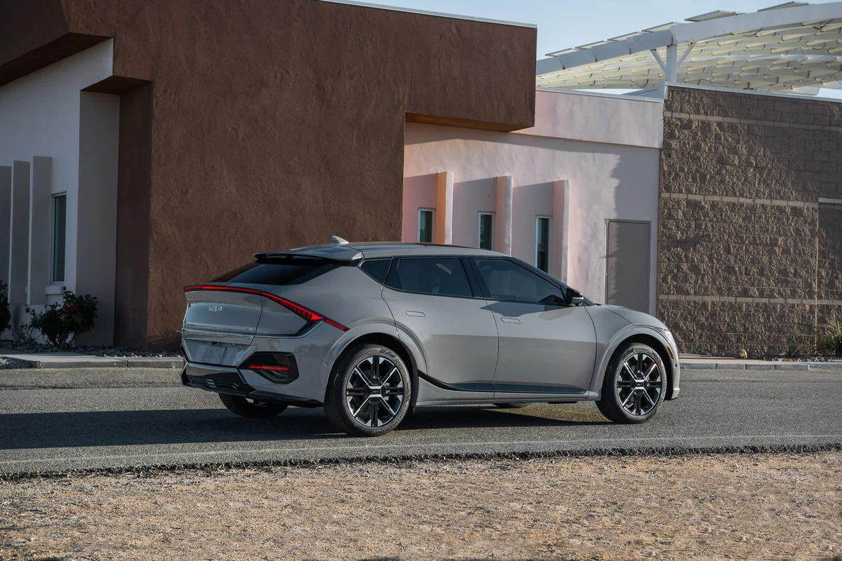 Silver 2026 Kia EV6 electric crossover parked in profile view against modern architecture with earth-tone buildings and clea…