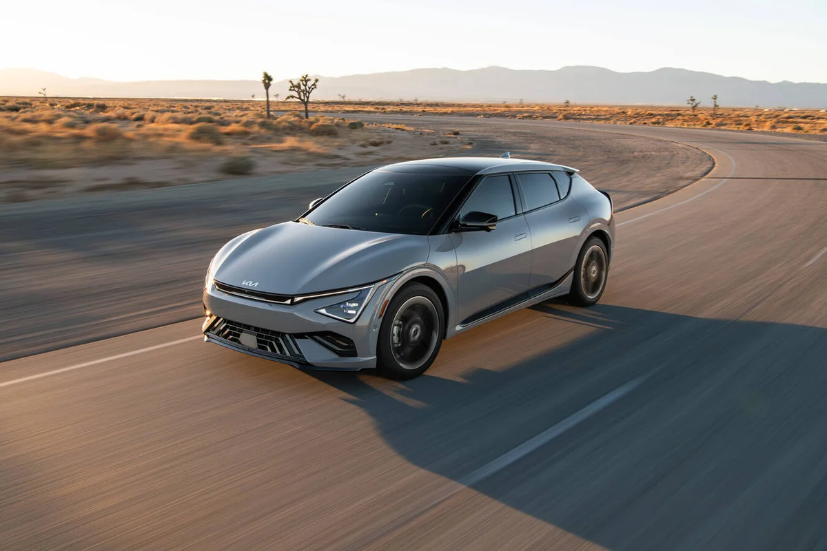 Silver 2026 Kia EV6 electric crossover driving on desert highway with mountains in background and Joshua trees visible acros…