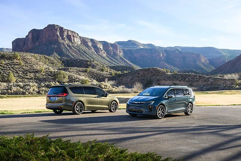 Two 2027 Chrysler Pacifica minivans parked side-by-side on desert road with red rock mountains in background