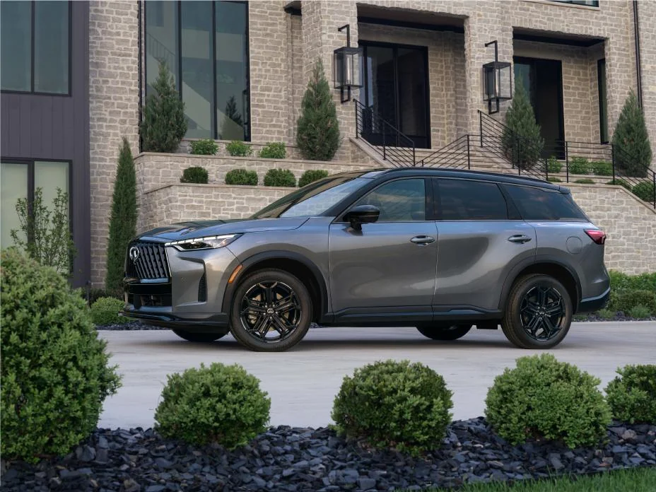 2027 Infiniti QX60 SPORT trim parked in front of modern brick building with landscaping, shown in side profile view