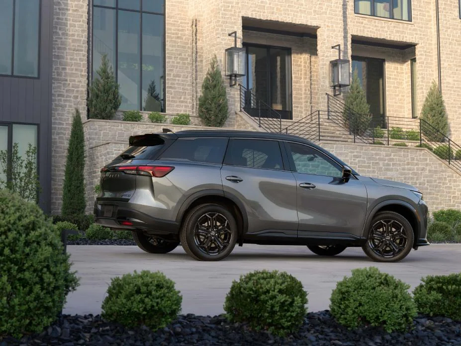 2027 Infiniti QX60 silver SUV parked in front of modern brick building with manicured landscaping