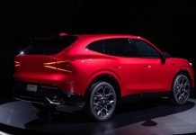 Acura Previews Next-Generation Hybrid SUV as RDX Replacement Bright red Acura hybrid SUV prototype displayed on dark stage, showcasing sleek profile with illuminated taillights and mode…