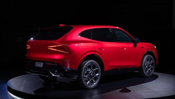 Bright red Acura hybrid SUV prototype displayed on dark stage, showcasing sleek profile with illuminated taillights and mode…