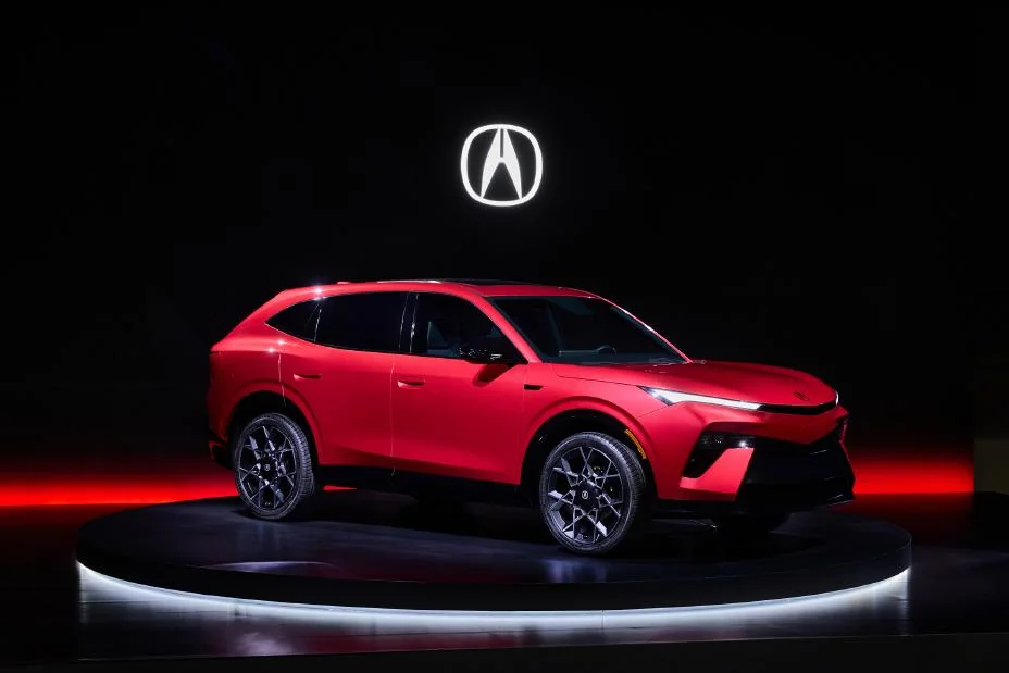 Red Acura hybrid SUV prototype on illuminated stage with Acura logo above, side profile view showcasing sleek design and all…