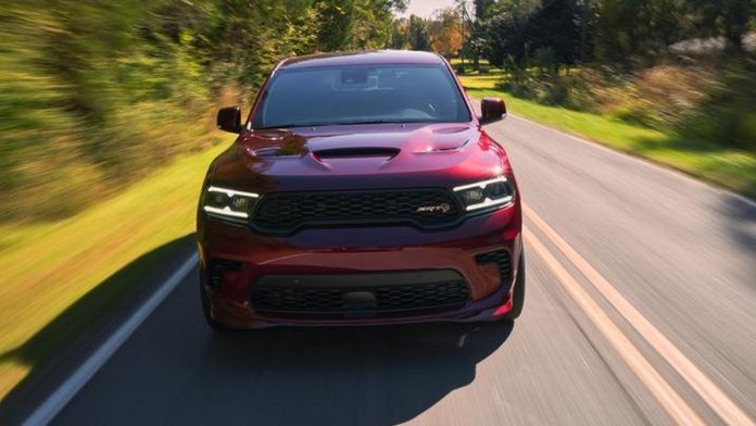 Red Dodge Durango Hellcat driving on a tree-lined highway, front view with motion blur showing performance capability.