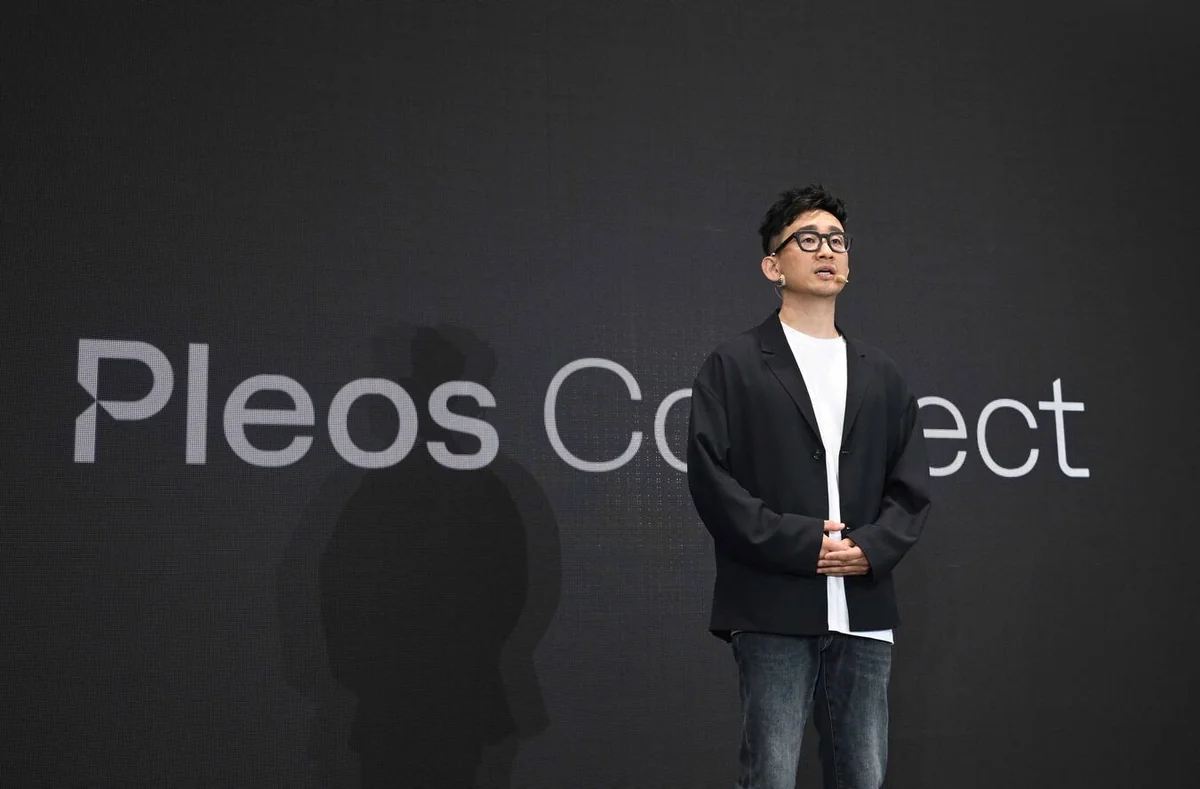 Man in business casual attire presenting Hyundai Pleos Connect infotainment system on stage with dark background display.