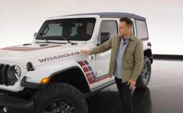 Jeep Wrangler America250 Edition Arrives This Summer With Captain America Shield and $2,095 Upcharge Man in tan jacket gestures toward white 2026 Jeep Wrangler America250 Edition with red and blue side graphics and exposed ho…