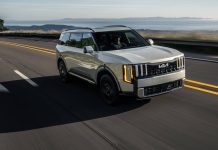 Kia Hybrids Surged 97 Percent in April While Competitors Shed Sales White Kia SUV driving on highway with coastal landscape visible in background, demonstrating Kia's hybrid vehicle growth in…