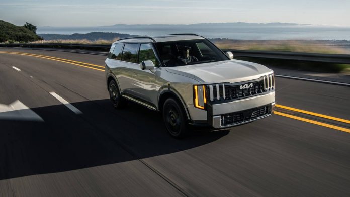 White Kia SUV driving on highway with coastal landscape visible in background, demonstrating Kia's hybrid vehicle growth in…